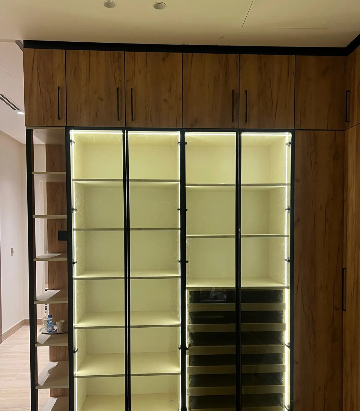Dressing room with lit glass-front shelving, walnut cabinets and glass shoe drawers