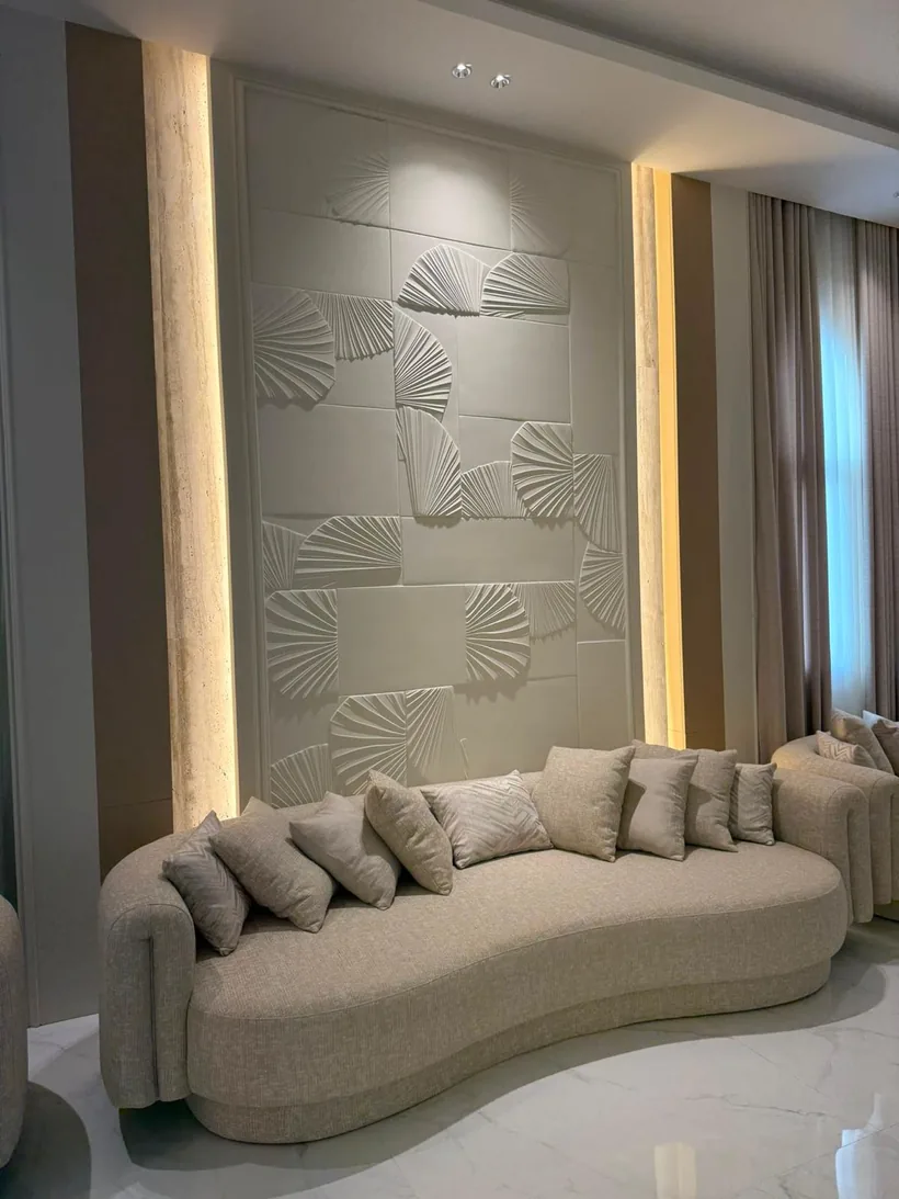 Feature wall with carved fan-shaped panels and hidden light, behind a curved sofa